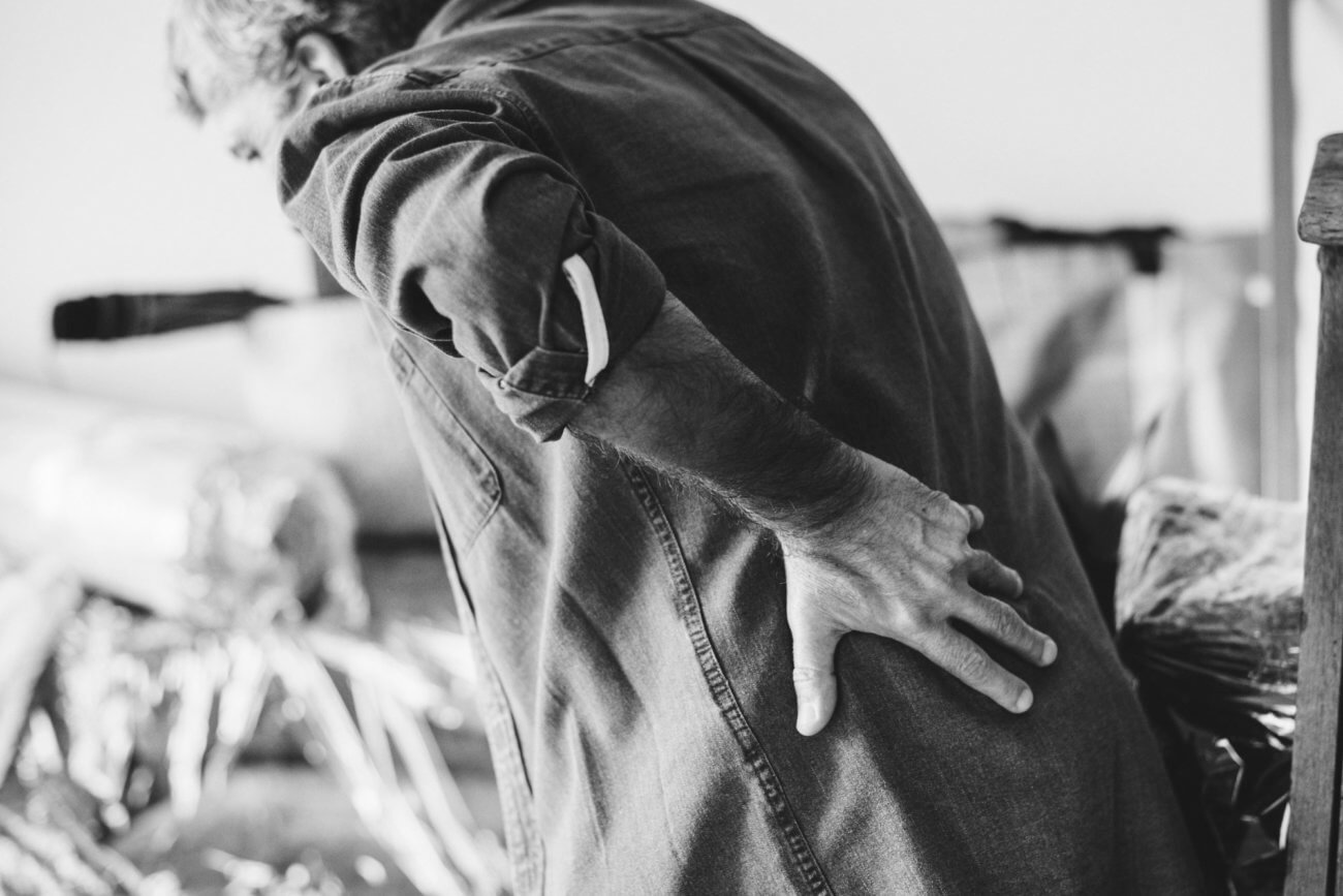 Black and white image of an adult male suffering from chronic low back pain leaning over and holding his back