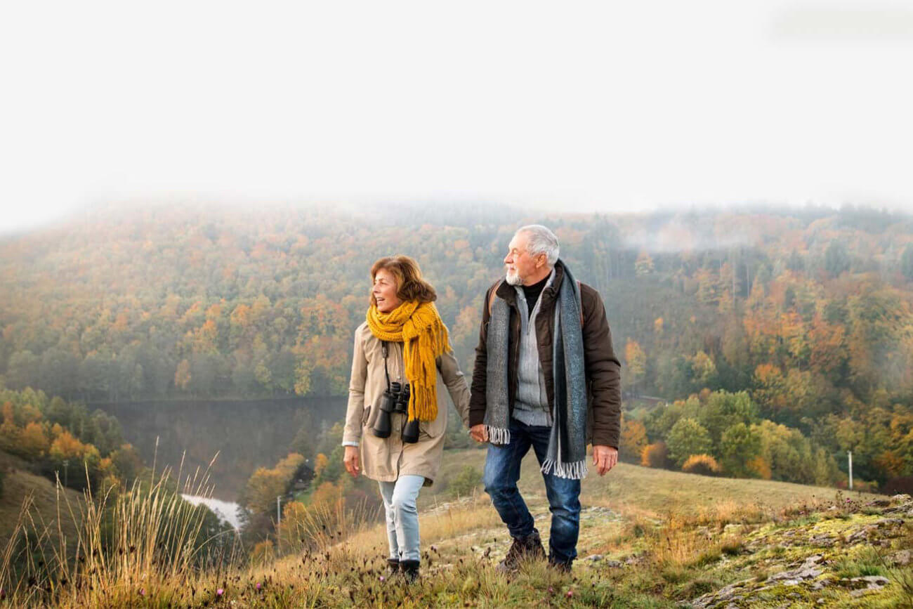 Senior couple walking on a hill with fall colors in the background