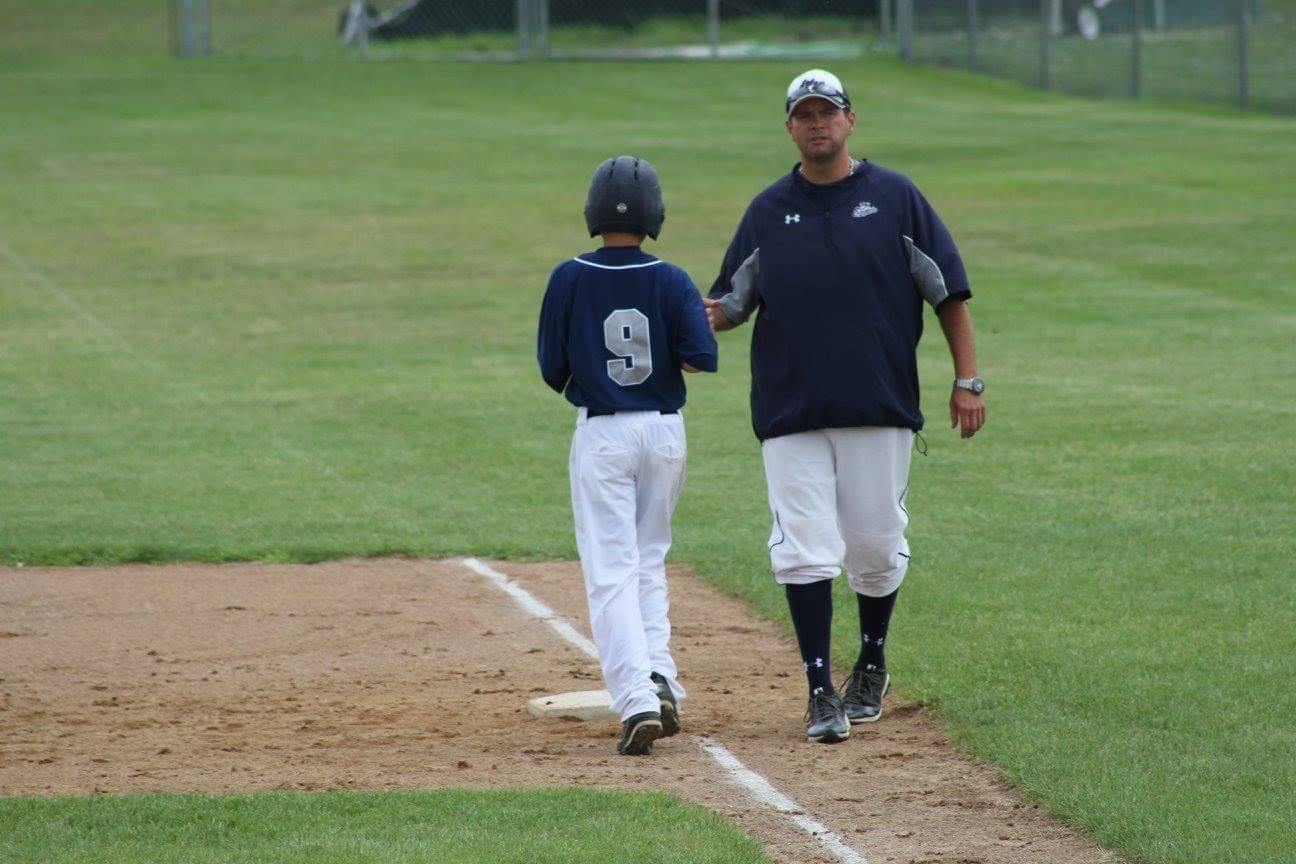 Troy Thielen high fiving a youth baseball player as the youth crosses first base