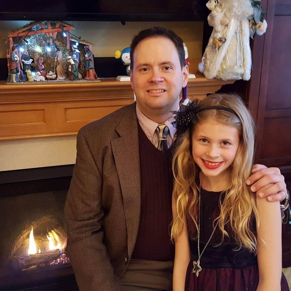 Troy Thielen and his daughter in formal wear posing in front of a fireplace