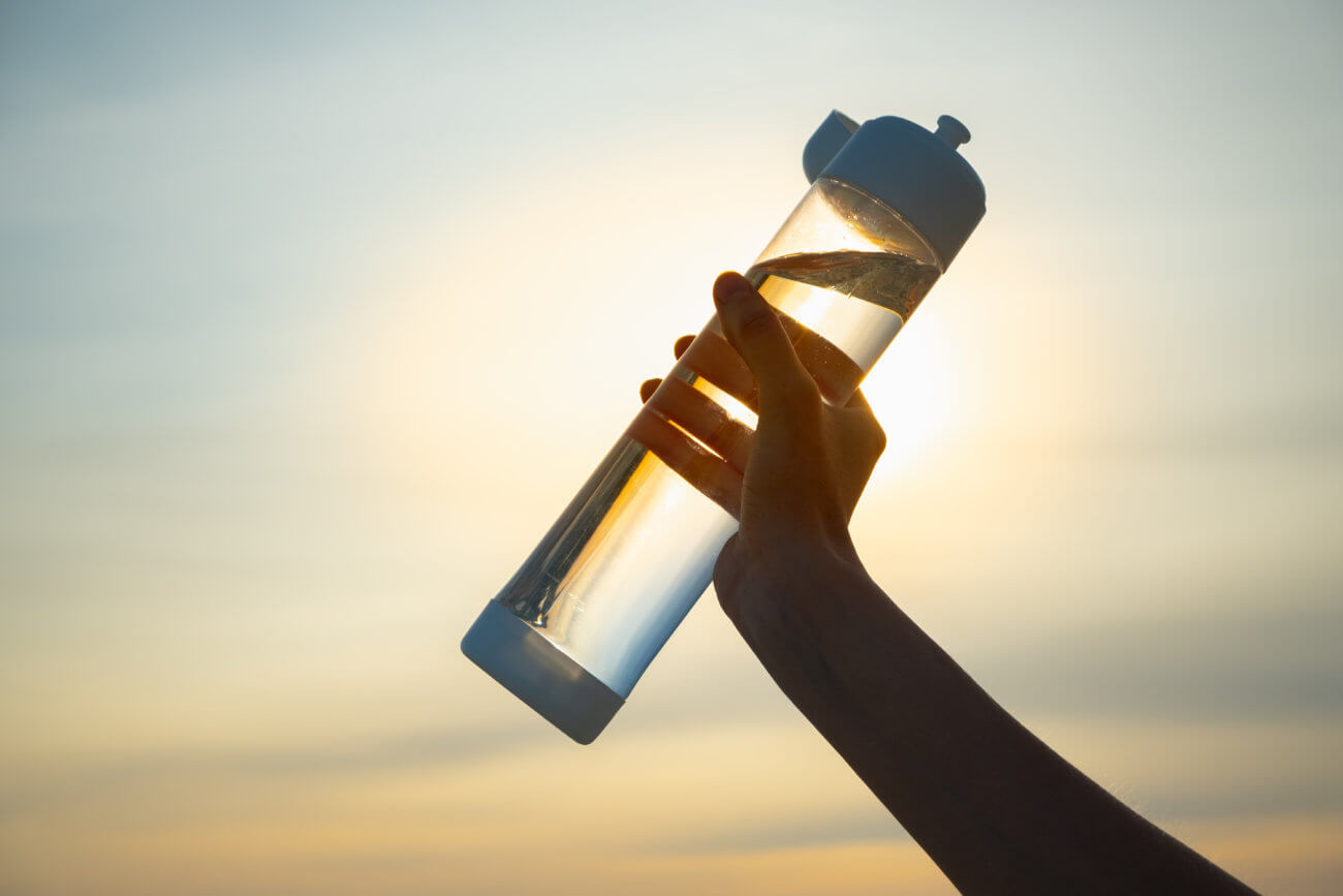 Human hand holding a water bottle against the setting sun