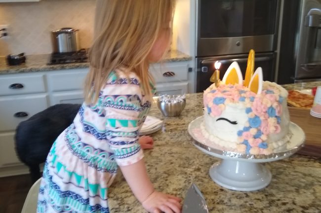 Girl blowing out candle on unicorn cake