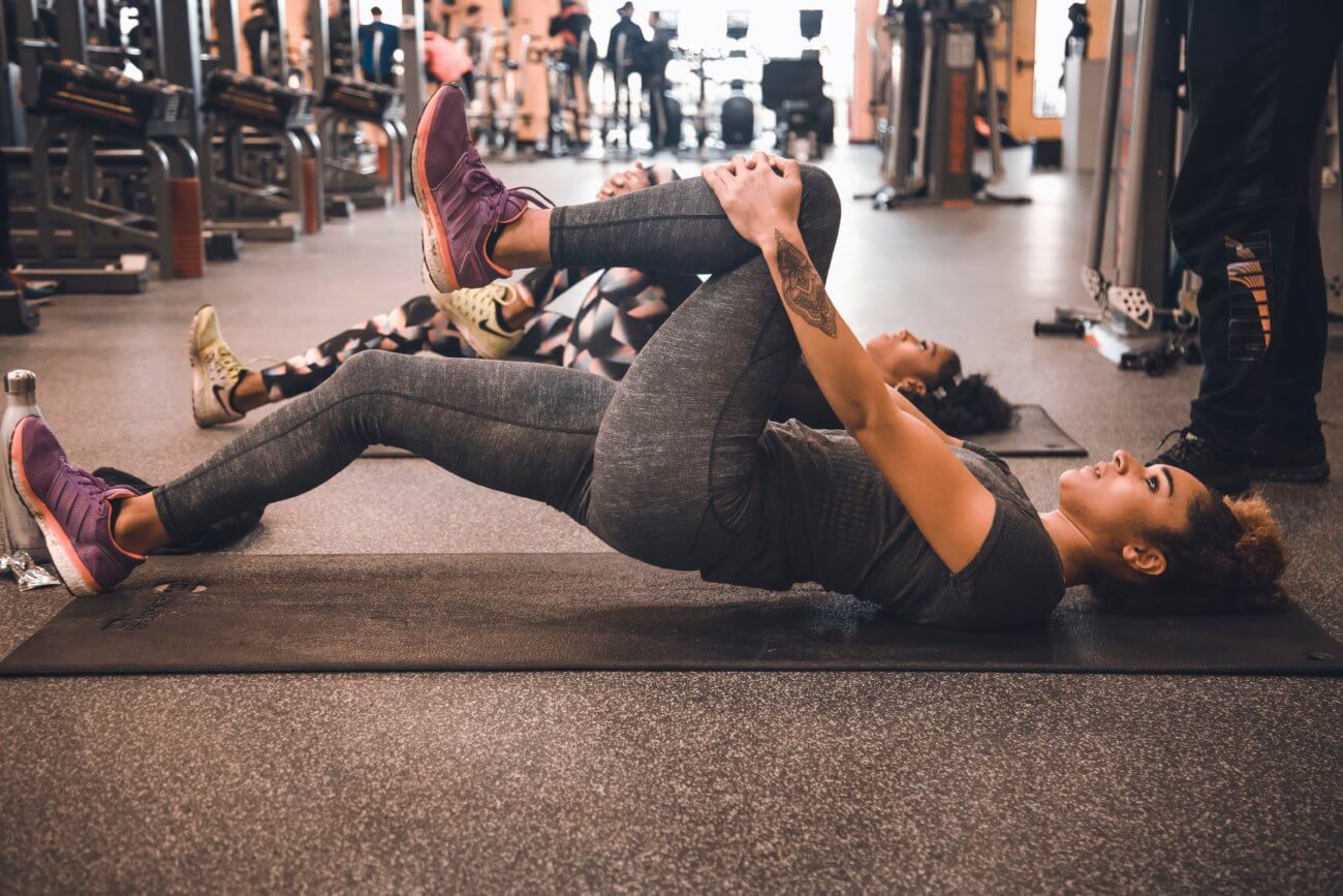 Young woman at a gym laying on a mat and stretching her leg