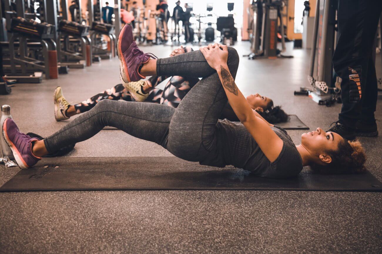 Woman laying on a mat stretching her leg at a gym