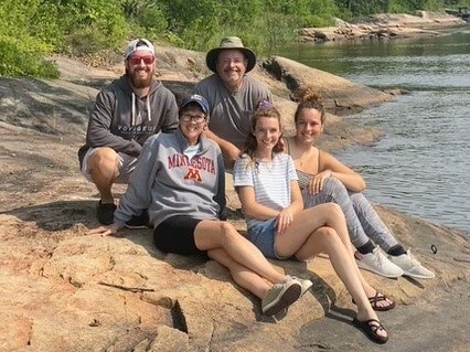 Lisa Brecht sitting with family on bank of a river