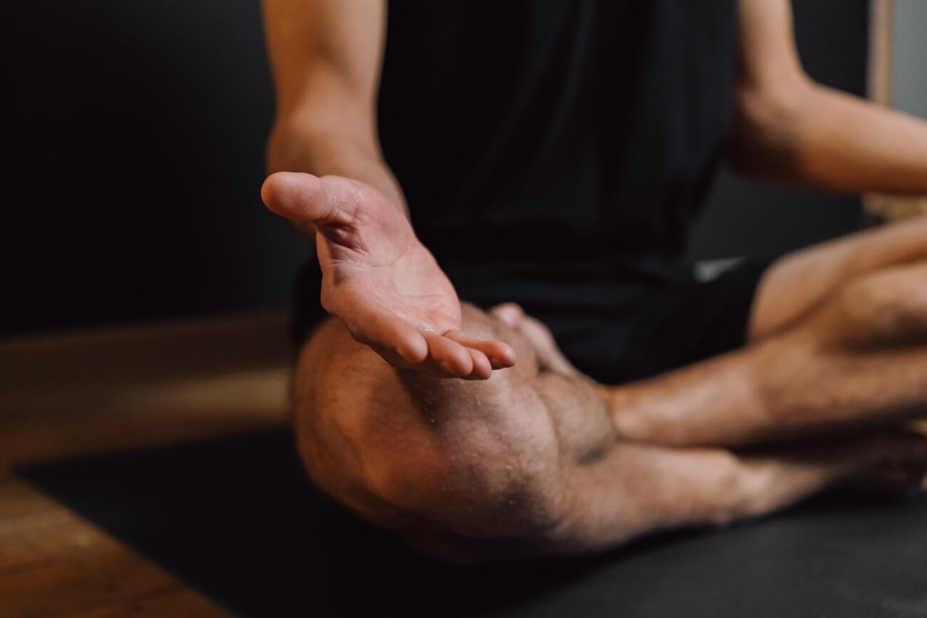 Man sitting with crossed legs and open palm resting on knee while meditating