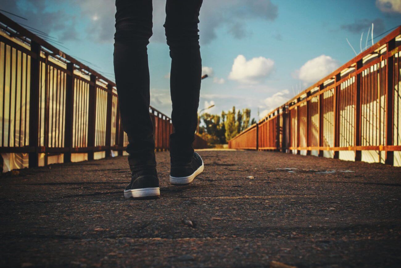 Rear view of man from the knees down walking across a bridge