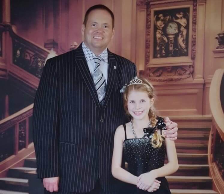 Troy Thielen and his daughter dressed in formal wear standing in front of a grand staircase