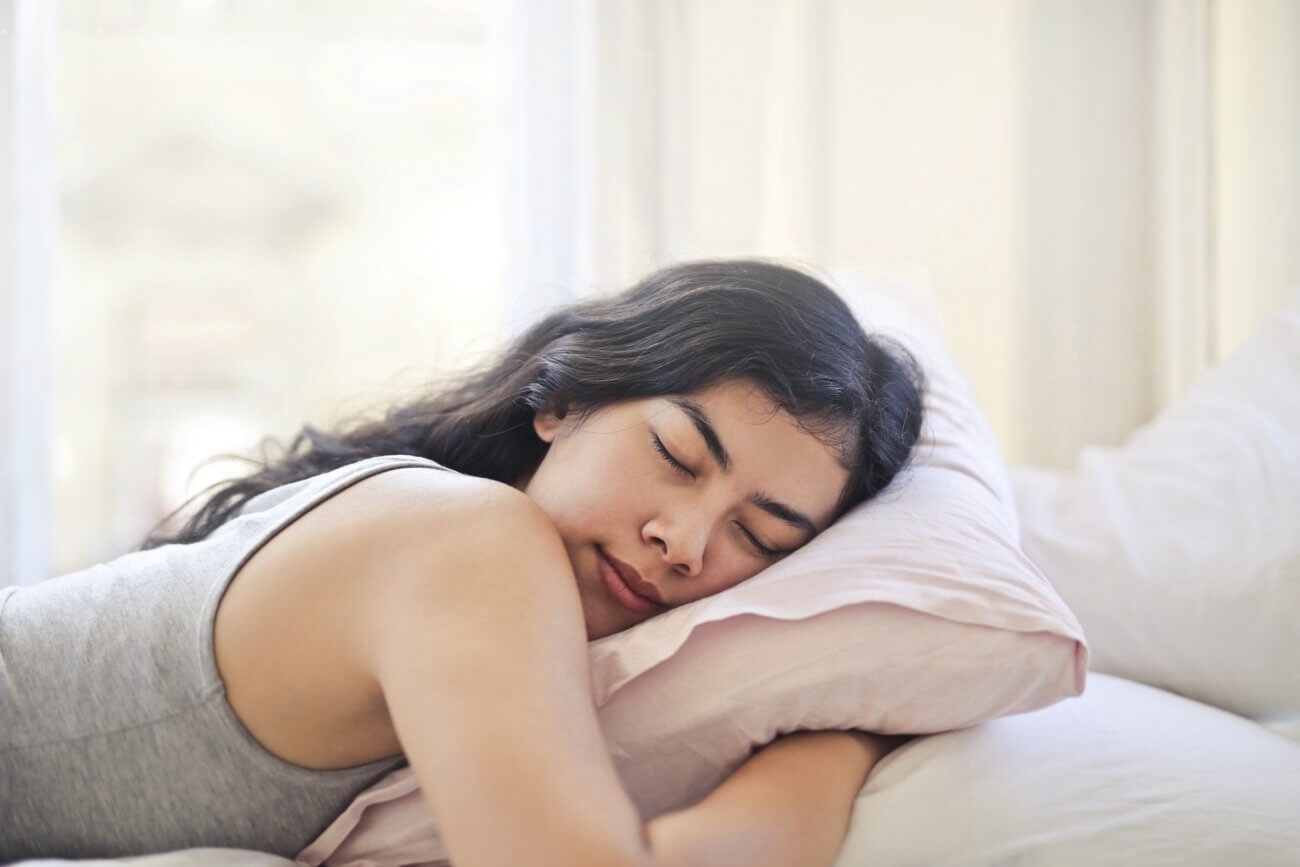 Dark haired woman sleeping in a bright room with her arms under her pillow