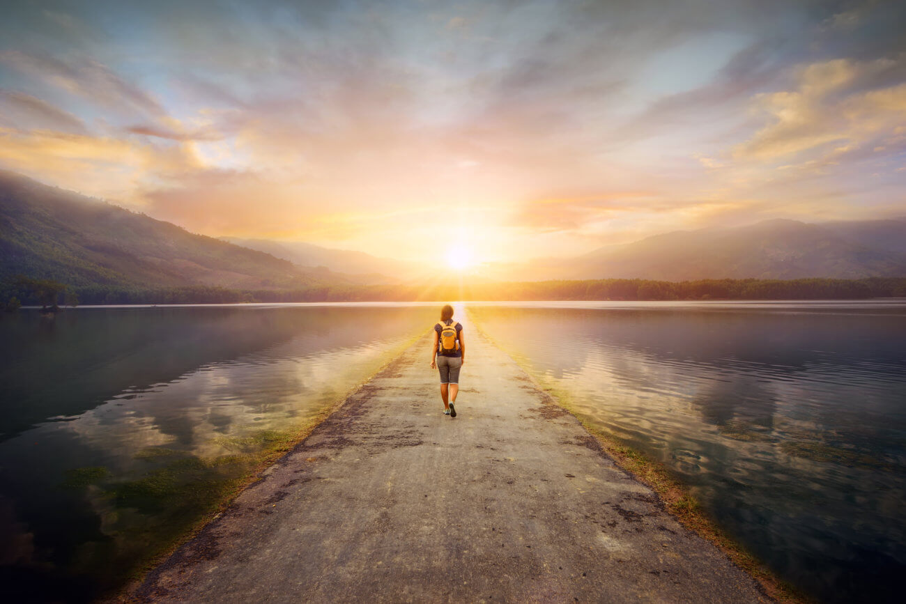 Woman walking down a straight road toward the sunrise