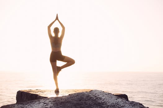 Woman doing yoga pose on a cliff overlooking sunrise-Chronic pain relief